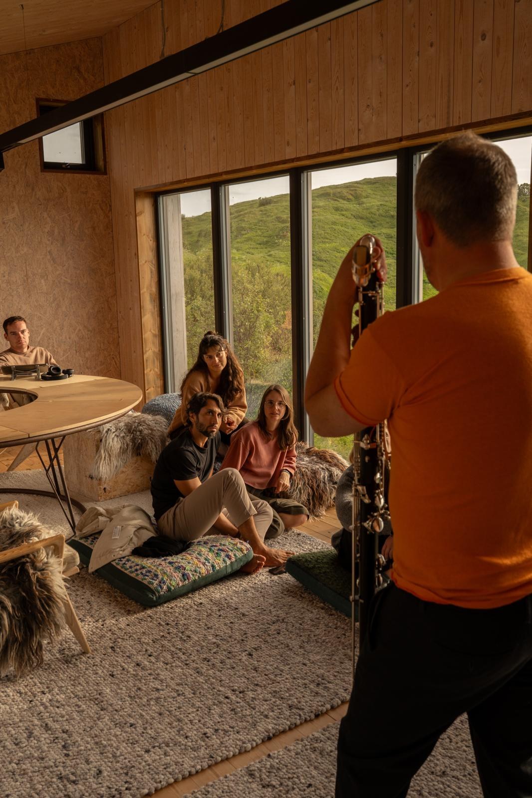 A small group being recorded playing a bass clarinet in a wood-panelled room overlooking the hills.