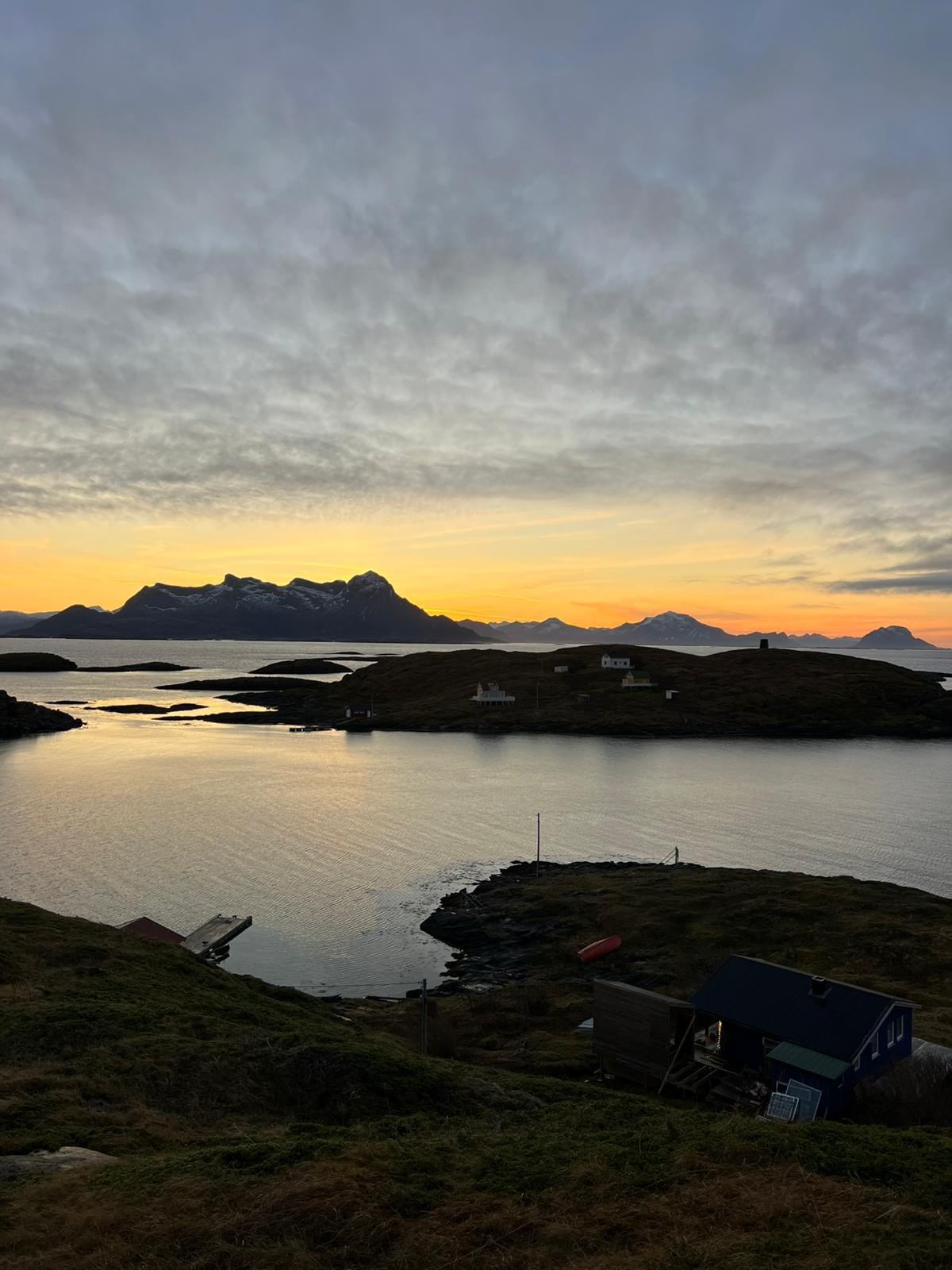 A sunset over the fjord at Fleinvær, Norway, with small island houses and a dock in the foreground.