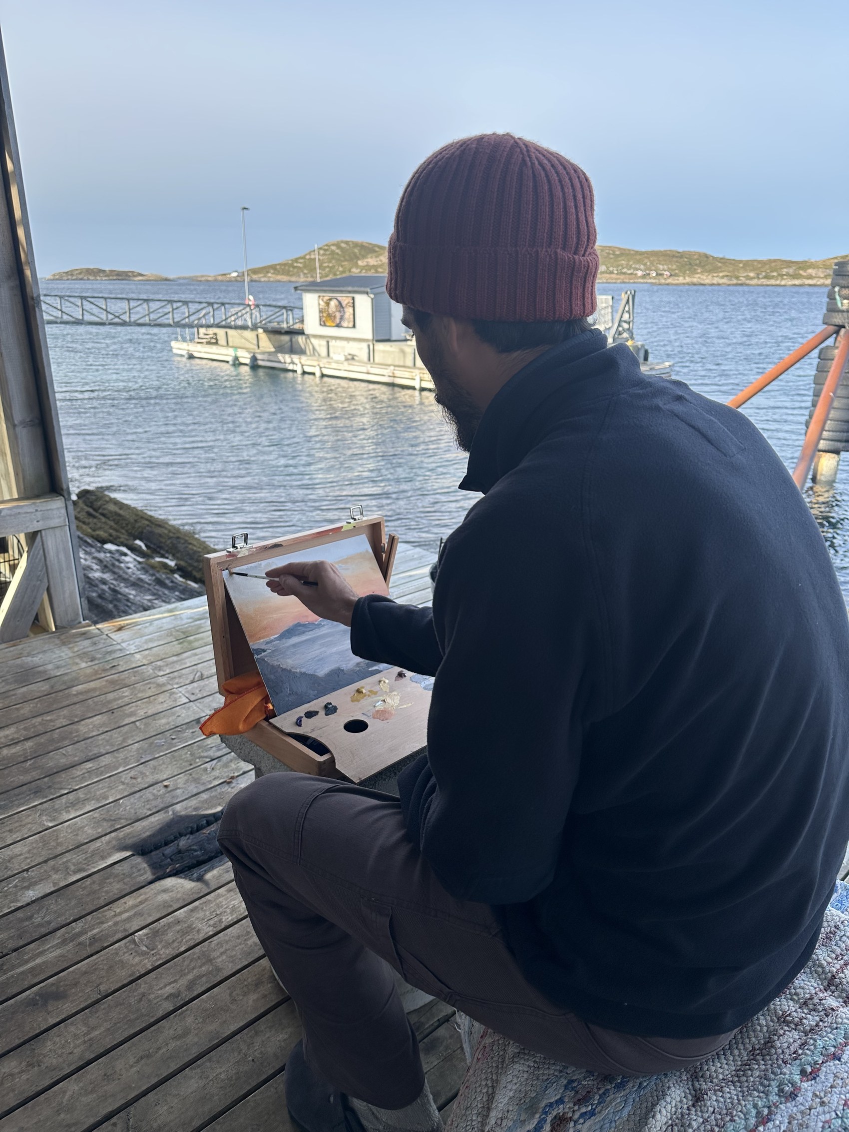 A painter working en plein air on the dock, looking out over the fjord.