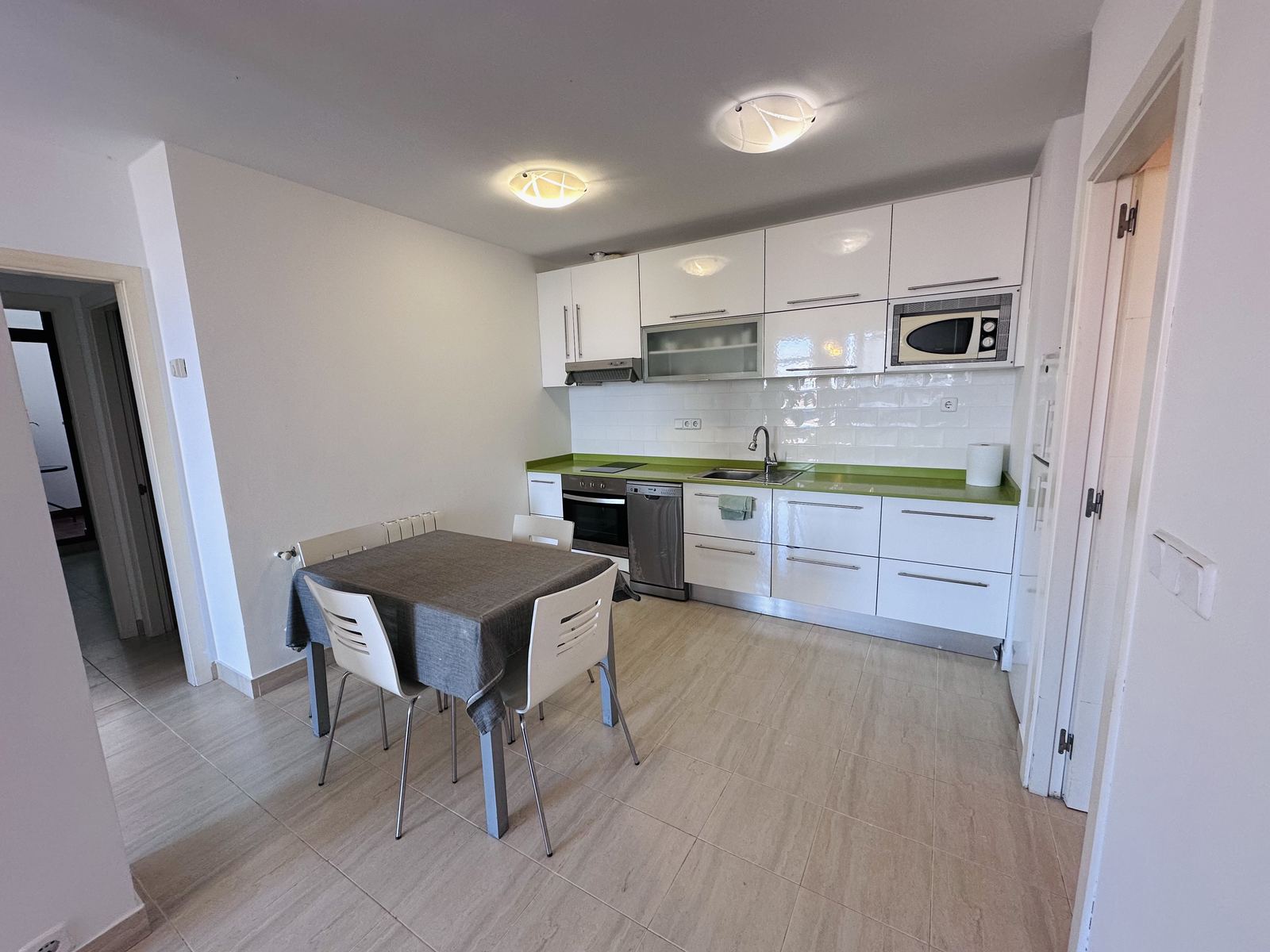 The apartment's kitchen and dining table, with white cabinets and a green worktop.