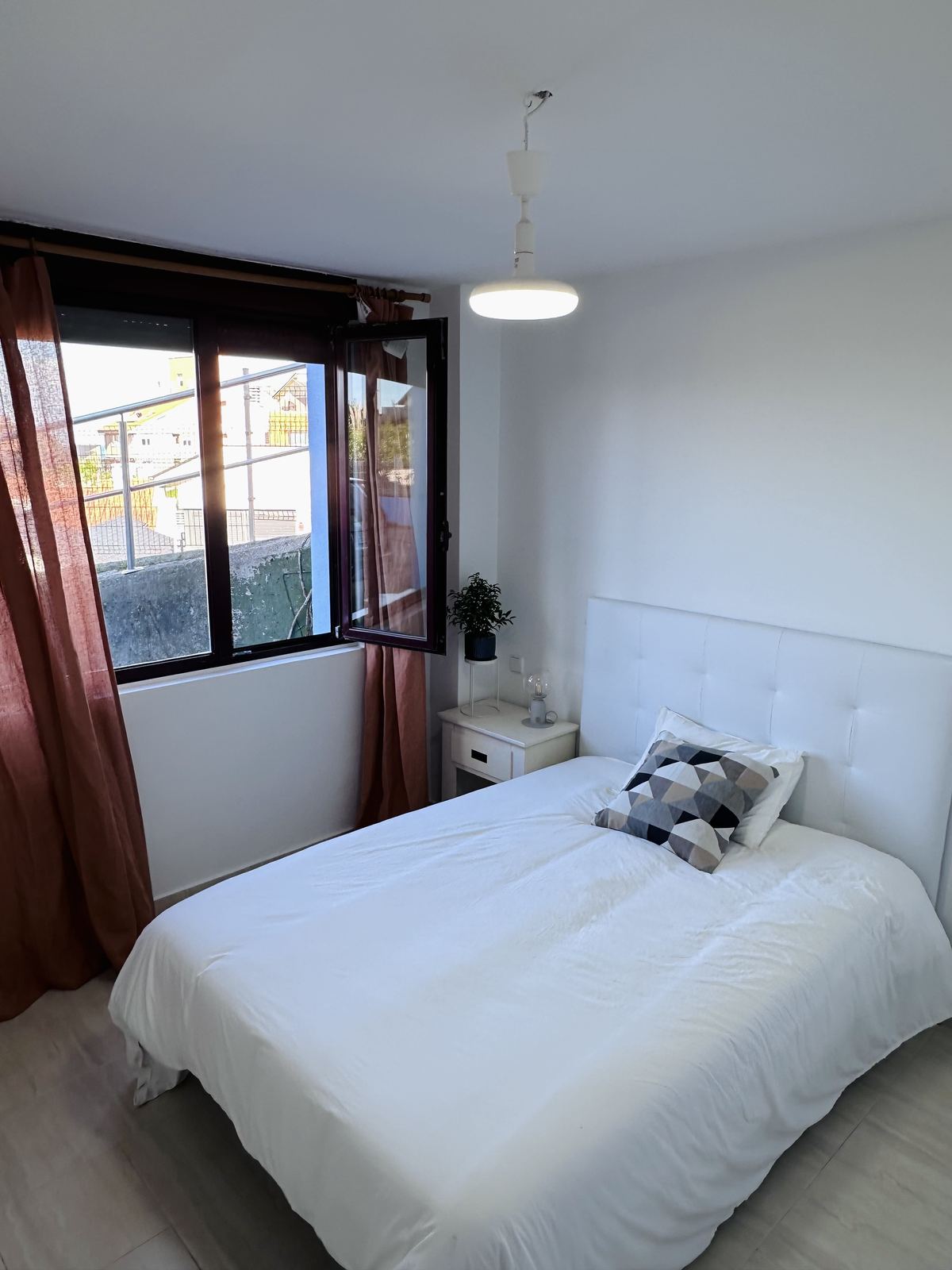 A second apartment bedroom, with a tufted white headboard and terracotta linen curtains.