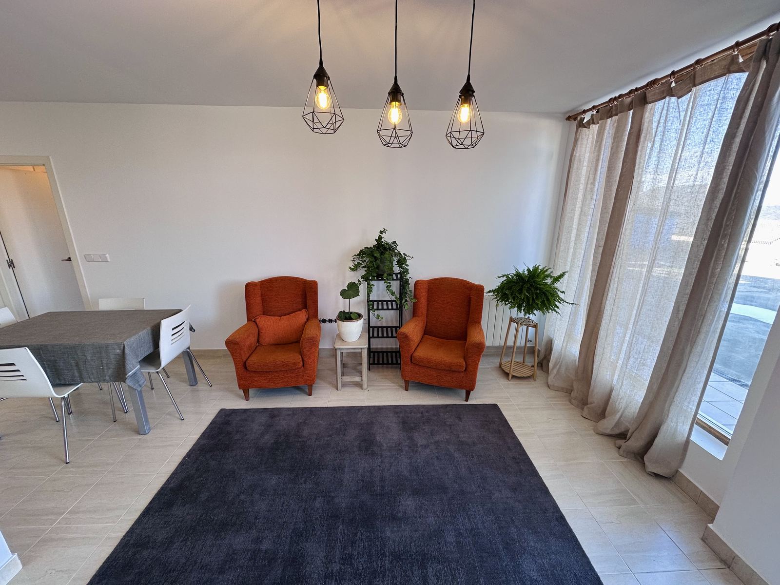 The apartment's sitting room, with two terracotta armchairs, a grey rug and long linen curtains.