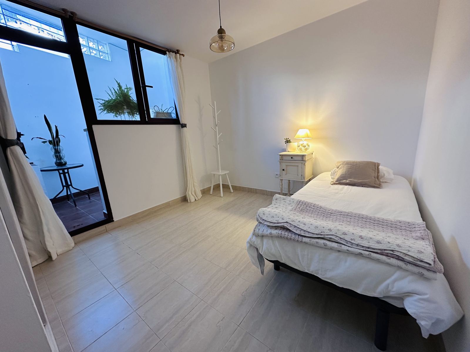 Apartment room 3: a single bed with a bedside lamp, and a glazed door onto the private studio patio.