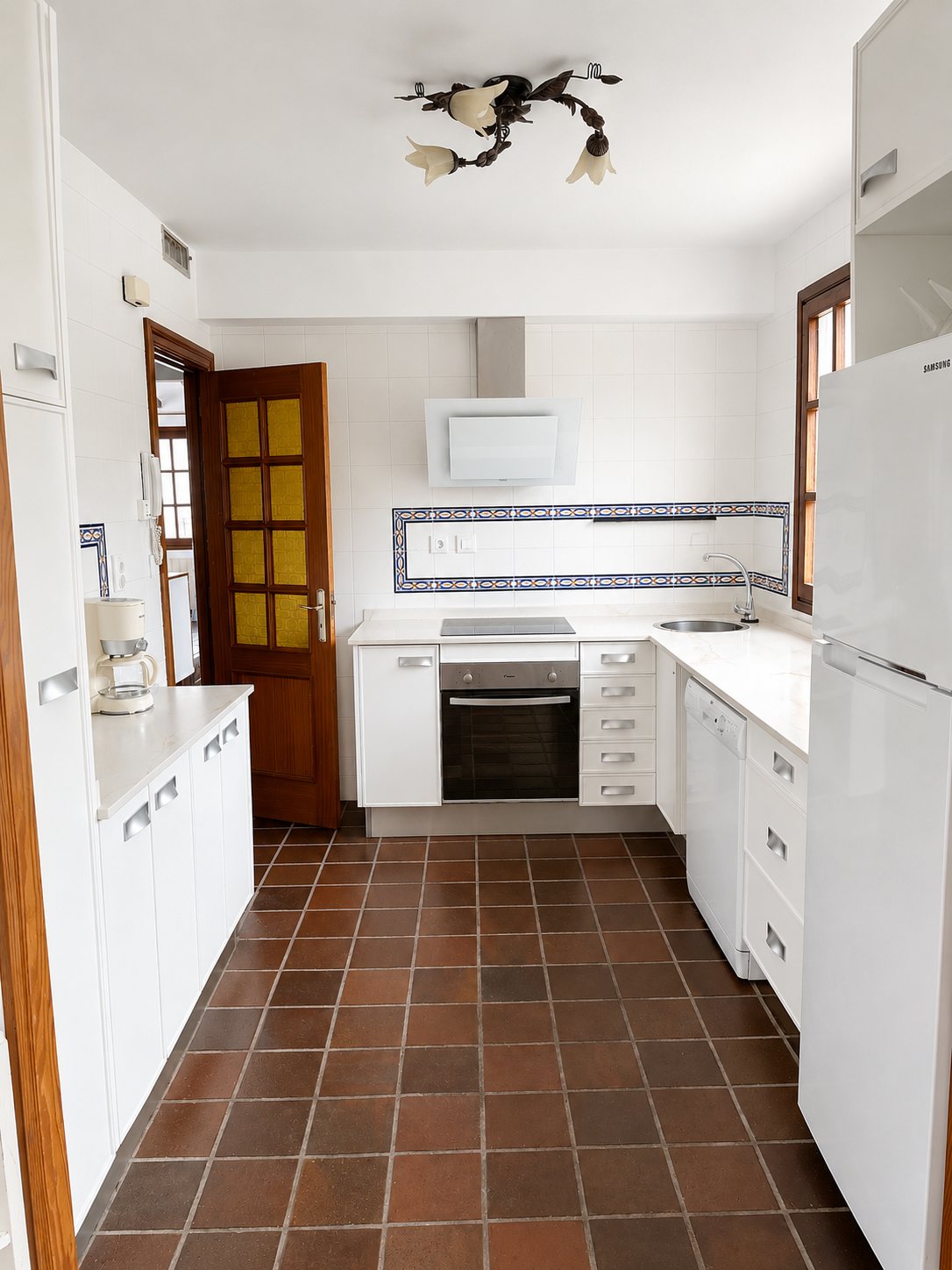 The white galley kitchen, with terracotta floor tiles.