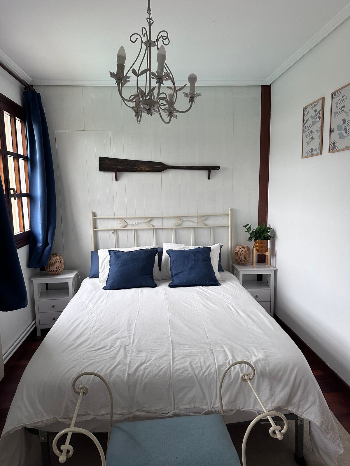 A bedroom with a white iron bed, navy cushions and a wooden oar on the wall behind the bed.