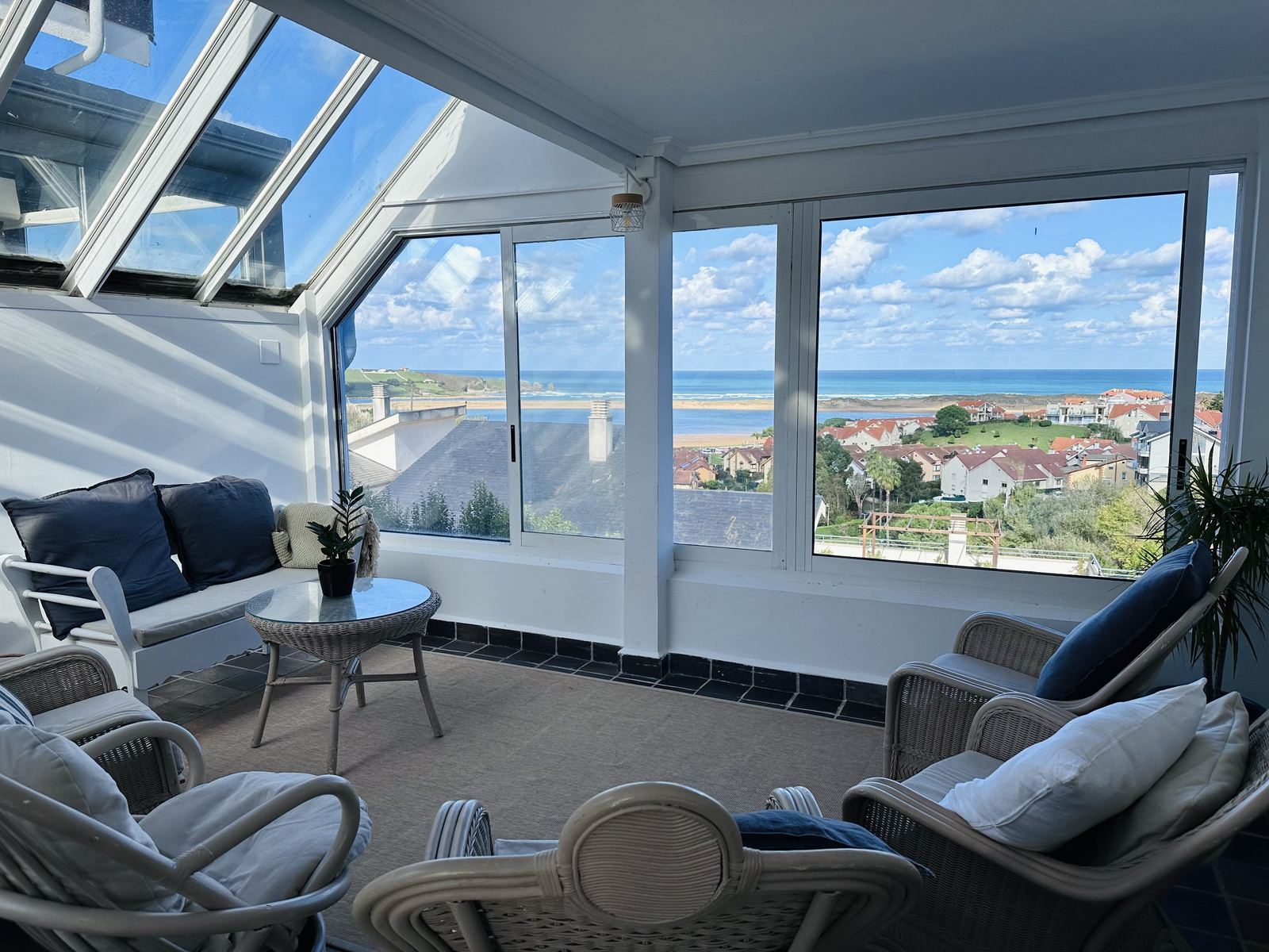 The sunroom at Casa Azul on a sunny day, with wicker armchairs and a wide view over the rooftops to the sea.