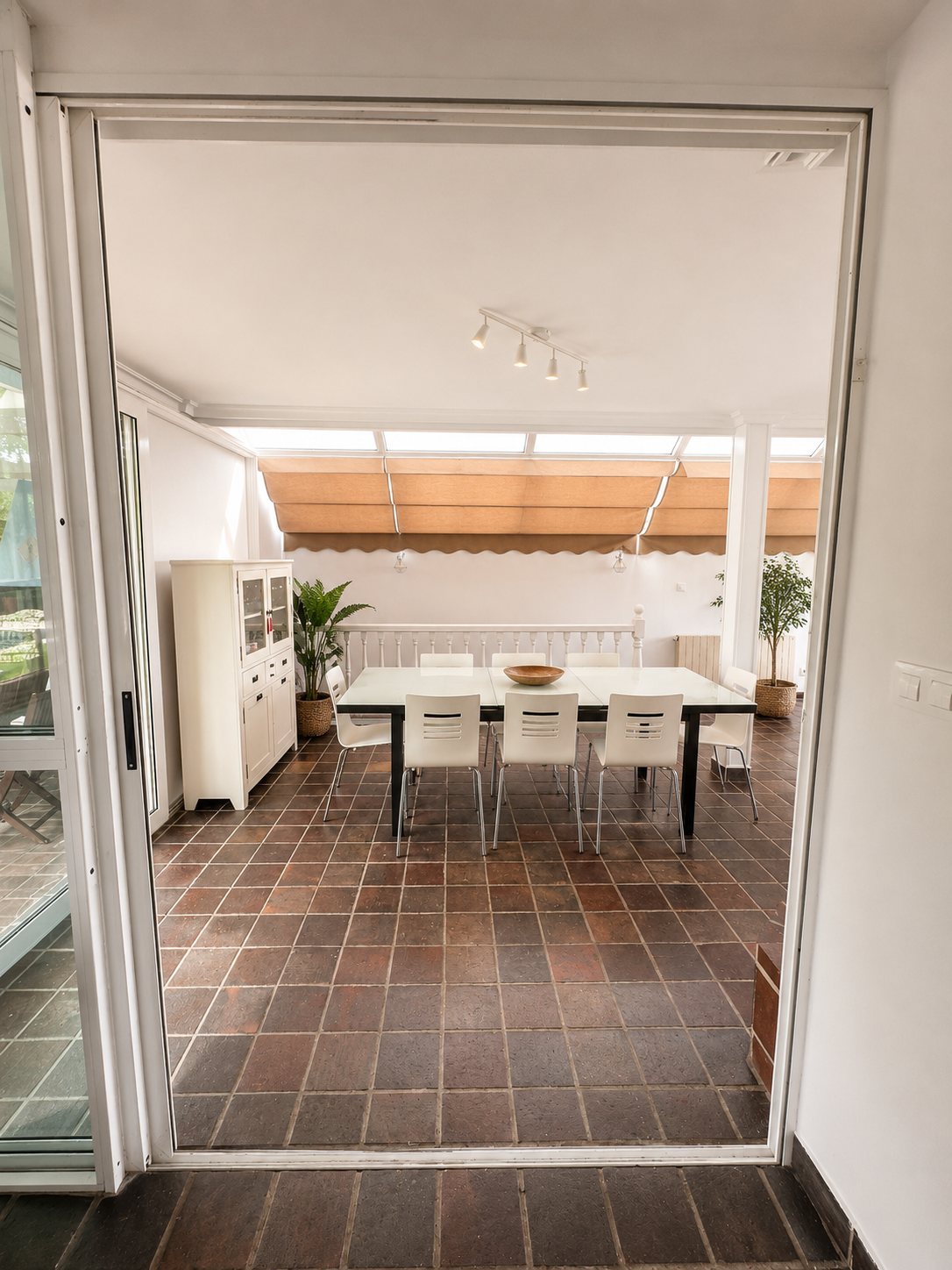 A covered terrace with a long dining table, seen through the sliding doors.