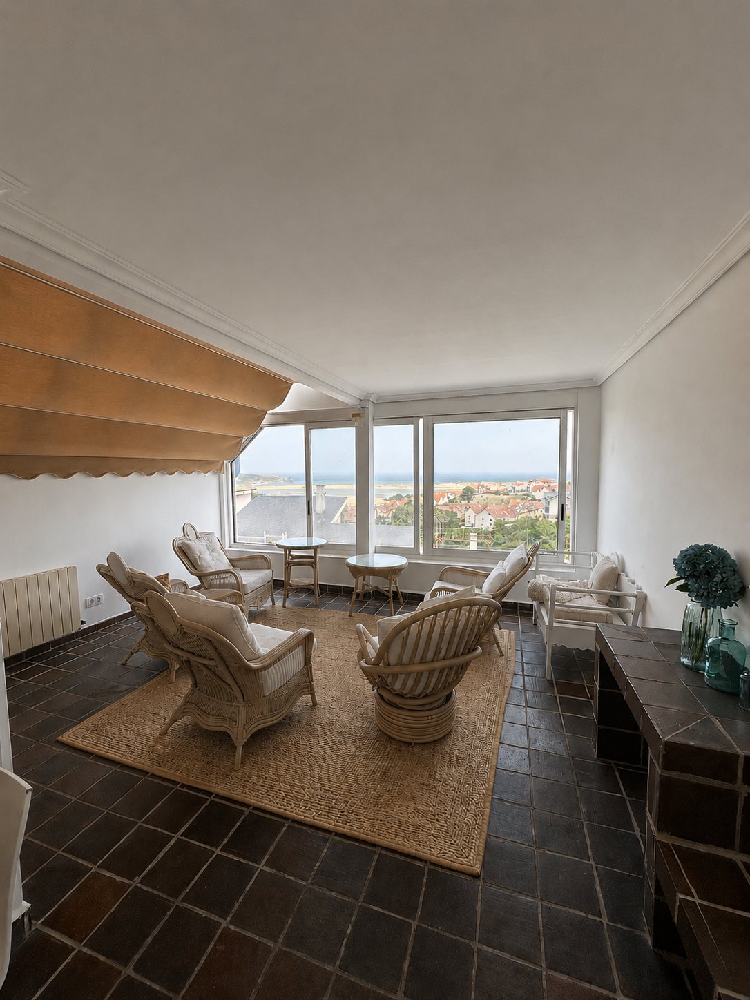 A sunroom with rattan chairs, overlooking the rooftops and the sea.
